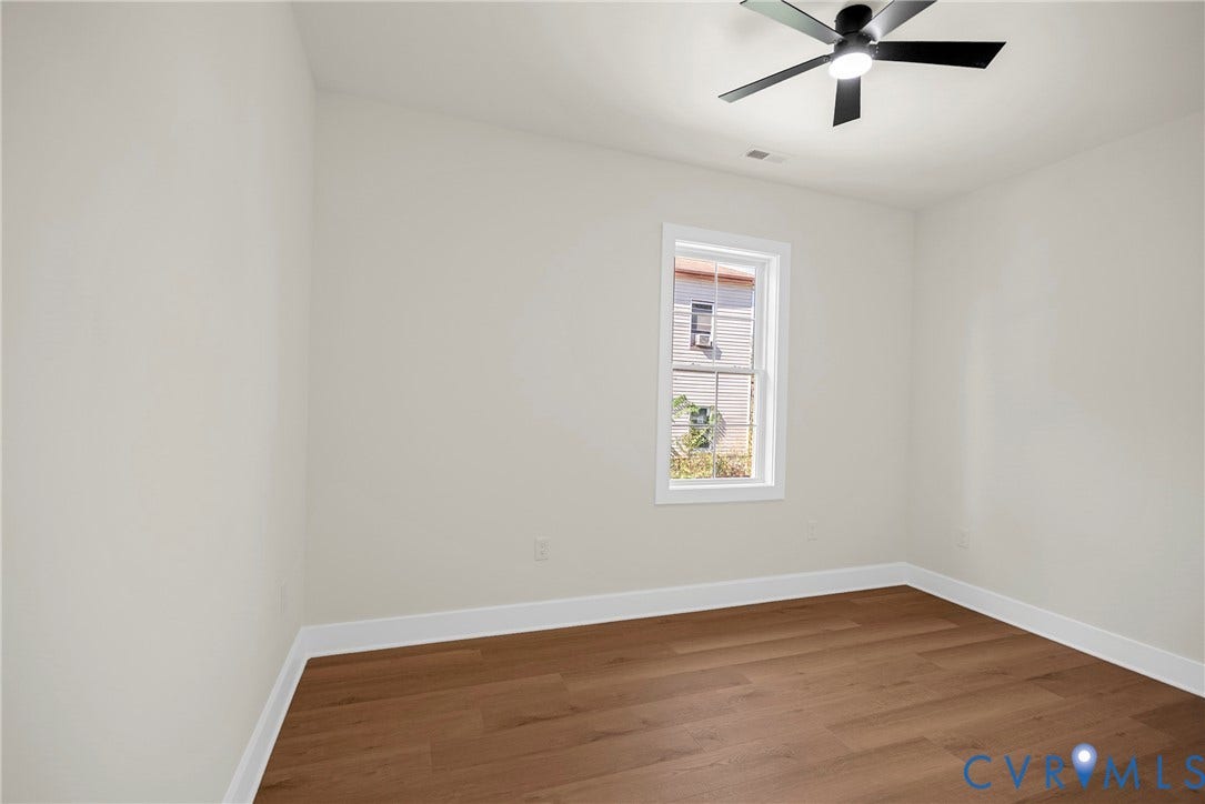 White walls, wood-finish flooring, white window trim, and a black ceiling fan with integrated lighting