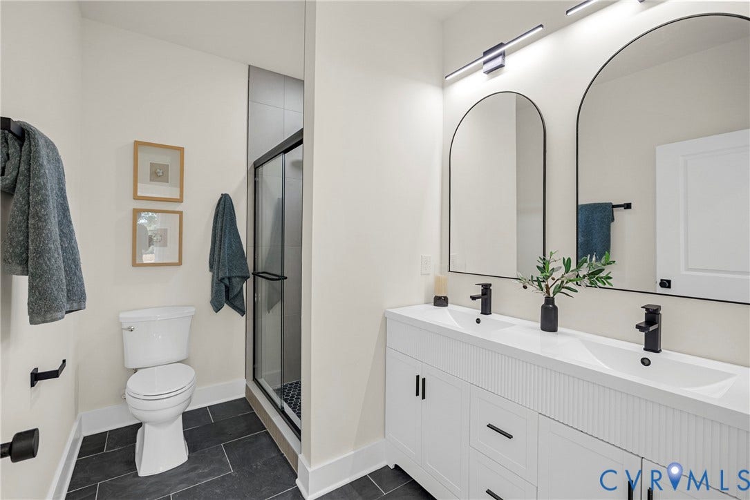 Double vanity with integrated sinks, two arched mirrors, glass-enclosed shower, and dark rectangular floor tiles