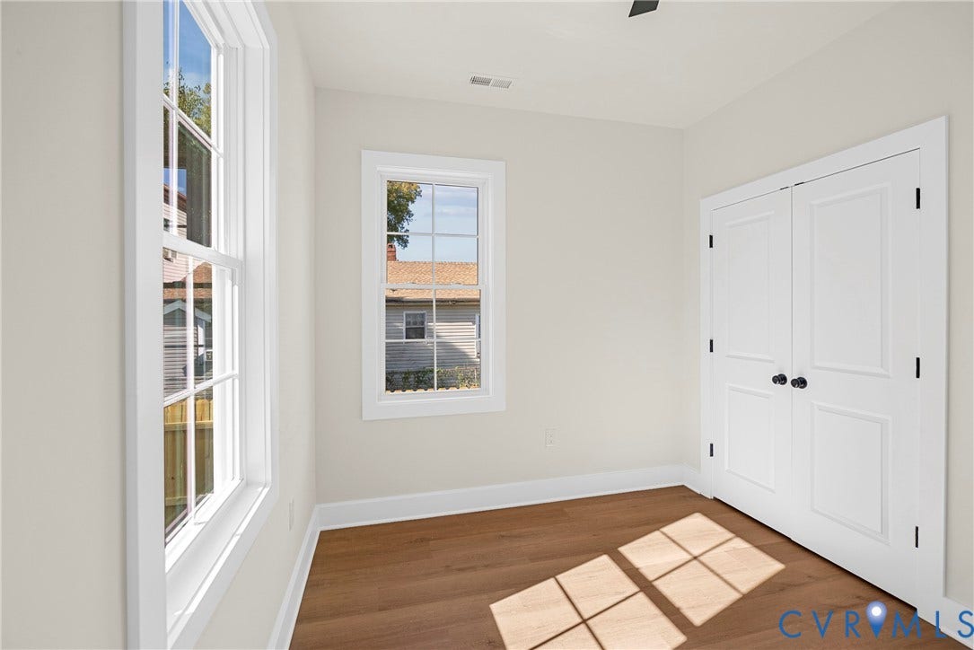 Smooth walls, wood-finish flooring, two windows with white trim, and a double-door closet with black hardware