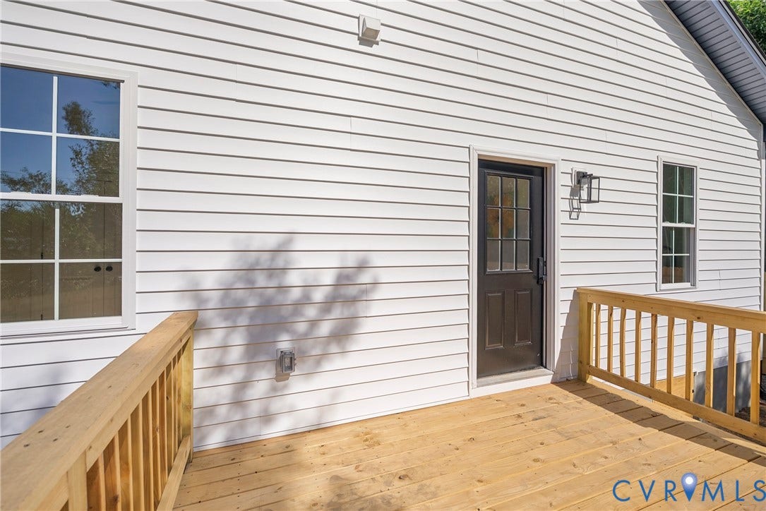 Exterior white horizontal siding with a wood deck, wood railing, and a dark entry door with a window
