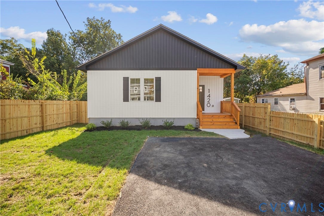 Exterior featuring dark vertical siding, light horizontal siding, natural wood-tone porch, paved driveway, and perimeter fencing