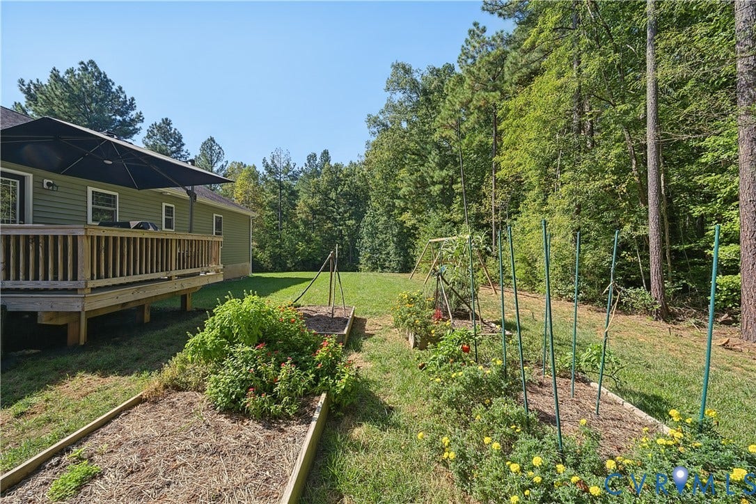 700 Manchester Road, Louisa, VA 23024 Rear exterior featuring a wooden deck with railing, light green siding, and multiple raised garden beds