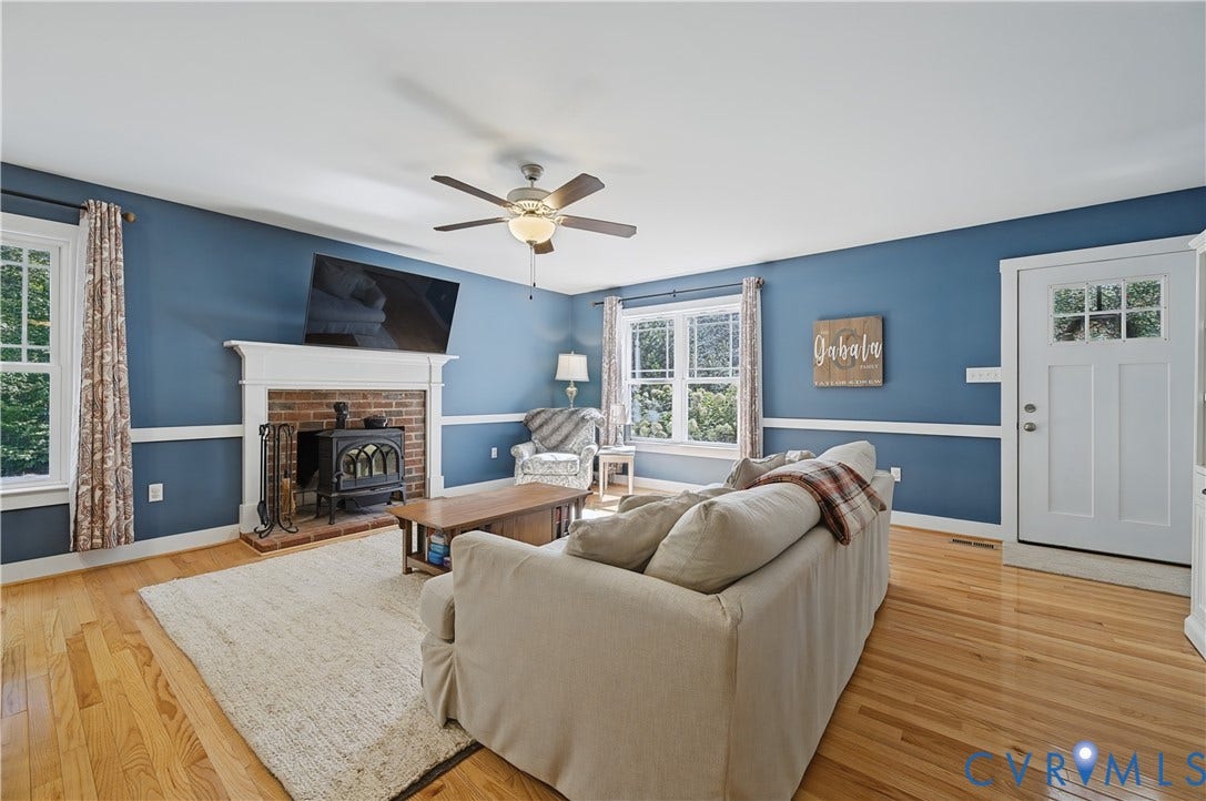 700 Manchester Road, Louisa, VA 23024 Brick fireplace with a wood-burning stove insert, wood-finish flooring, multiple windows, and a ceiling fan