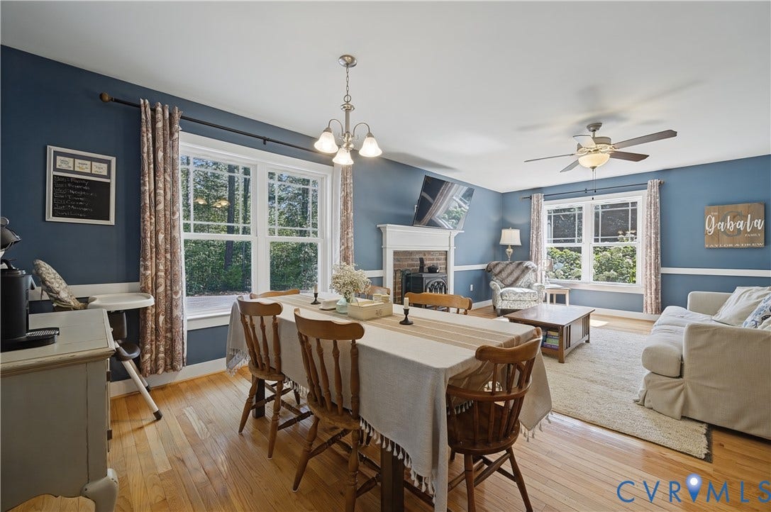 700 Manchester Road, Louisa, VA 23024 Hardwood-finish flooring throughout, two large windows, a ceiling fan with integrated lighting, a fireplace with a brick surround, and a coordinating chandelier