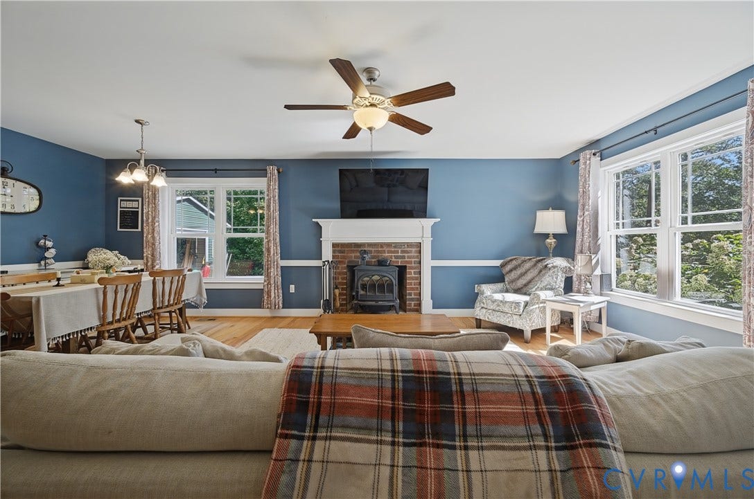 700 Manchester Road, Louisa, VA 23024 Hardwood flooring, a wood-burning stove with a brick surround, a mantel, a ceiling fan, and multiple windows