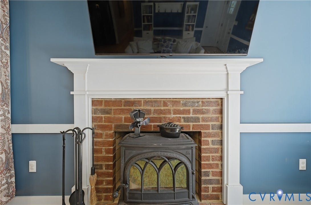 700 Manchester Road, Louisa, VA 23024 Brick fireplace with a white wood mantel, featuring a wood-burning stove and wainscoting
