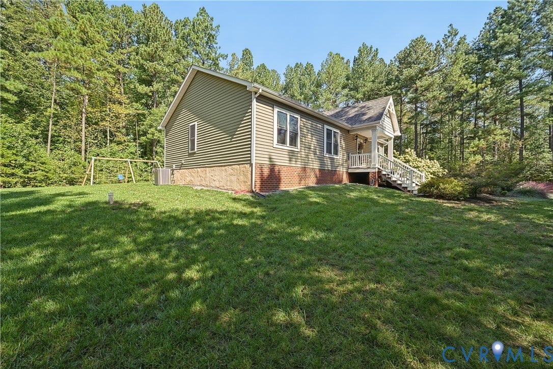 700 Manchester Road, Louisa, VA 23024 Fiber cement siding, brick foundation, covered porch with white railings, mature trees, and a spacious lawn