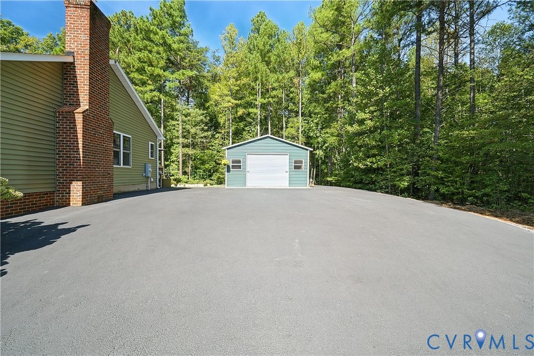 700 Manchester Road, Louisa, VA 23024 Expansive asphalt driveway, brick chimney, green siding, and a detached outbuilding with a garage door