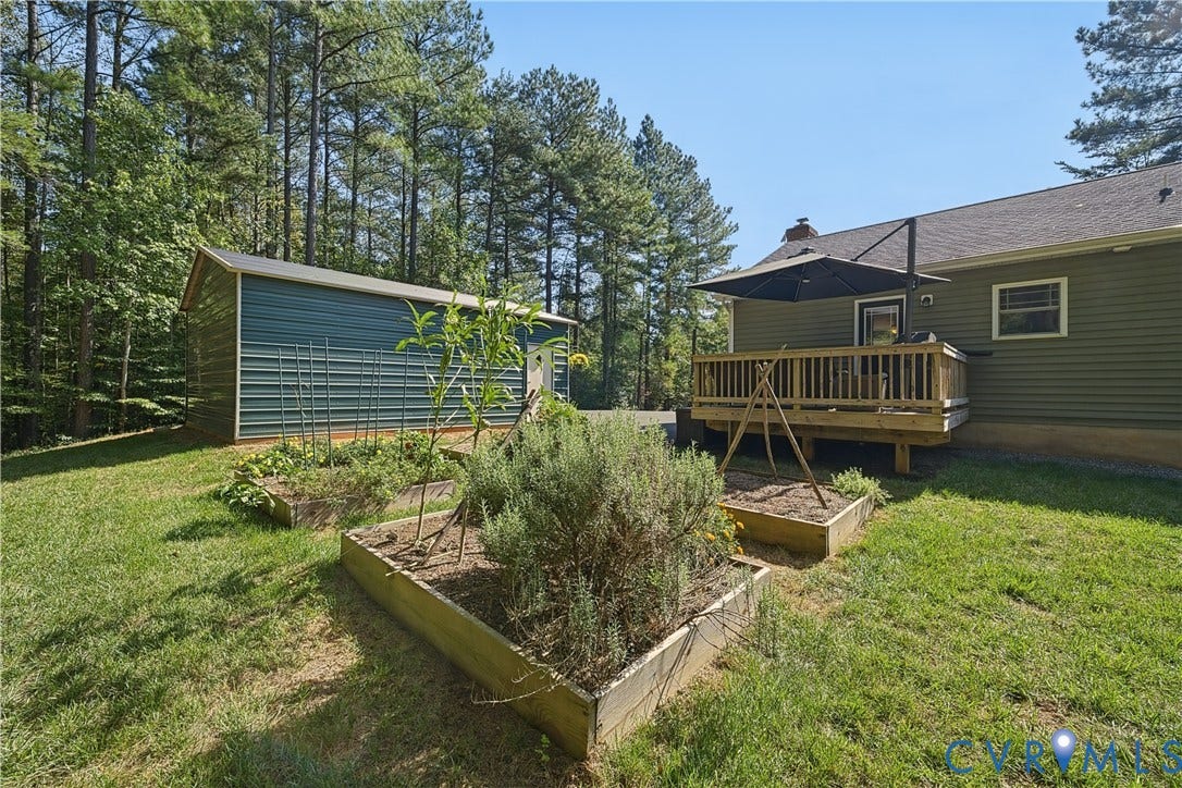 700 Manchester Road, Louisa, VA 23024 Expansive backyard featuring a wood deck, multiple raised garden beds, a metal-sided accessory building, and mature trees