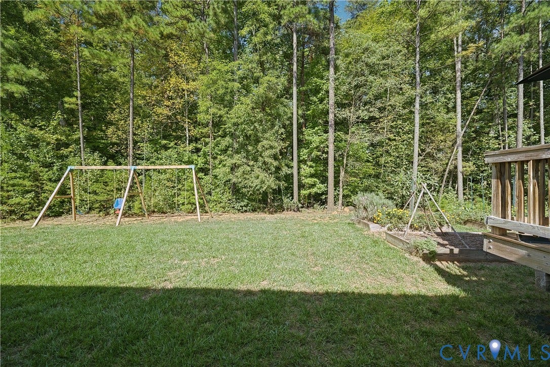 700 Manchester Road, Louisa, VA 23024 Expansive grassy yard with a wooden swing set, raised garden beds, and mature trees providing a natural backdrop