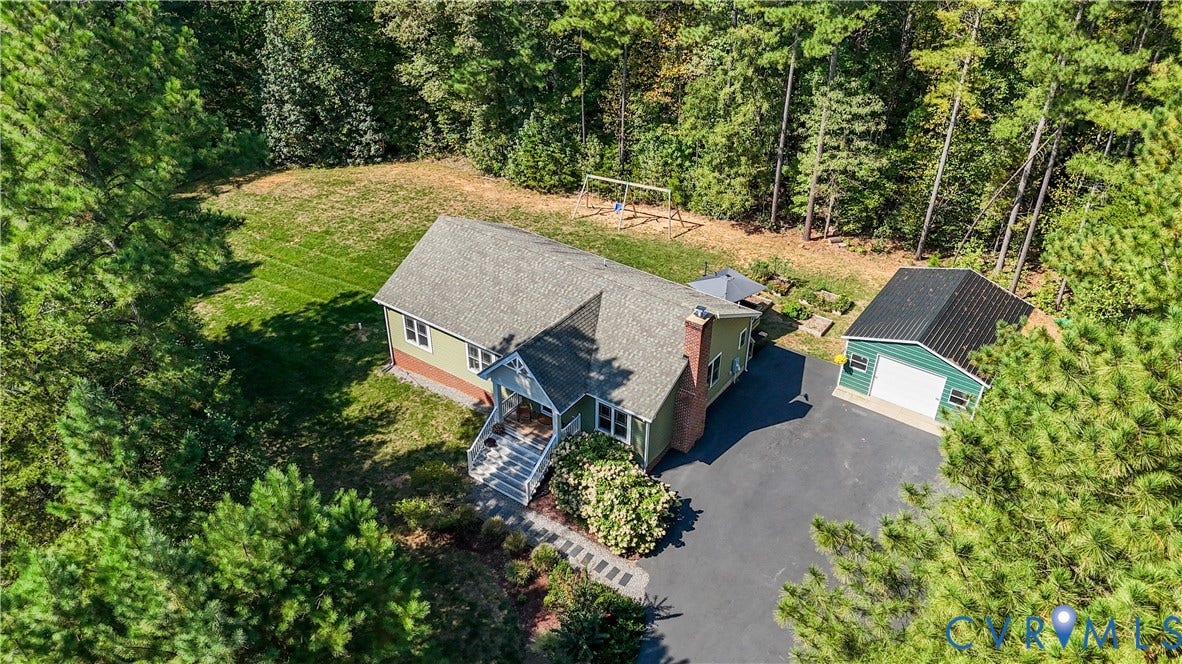700 Manchester Road, Louisa, VA 23024 Residential property with a light green exterior, an attached front porch with white railings, a paved driveway, a separate green outbuilding with a white garage door, and a surrounding wooded landscape