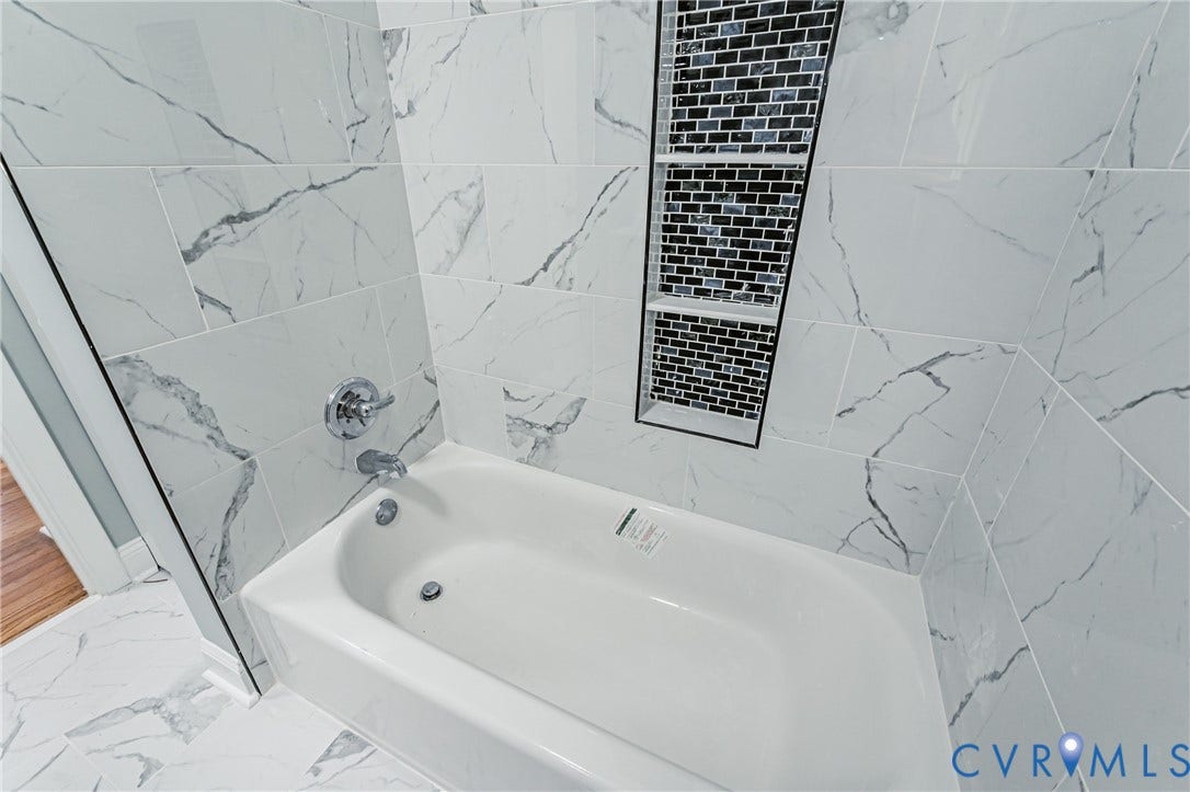 1724 Alaska Drive, Richmond, VA 23224 White bathtub with chrome fixtures, surrounded by white and gray veined tile