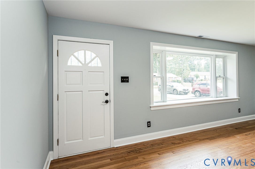 1724 Alaska Drive, Richmond, VA 23224 Light gray wall paint, wood-finish flooring, white trim, white paneled entry door with an arched window, and a large bay window