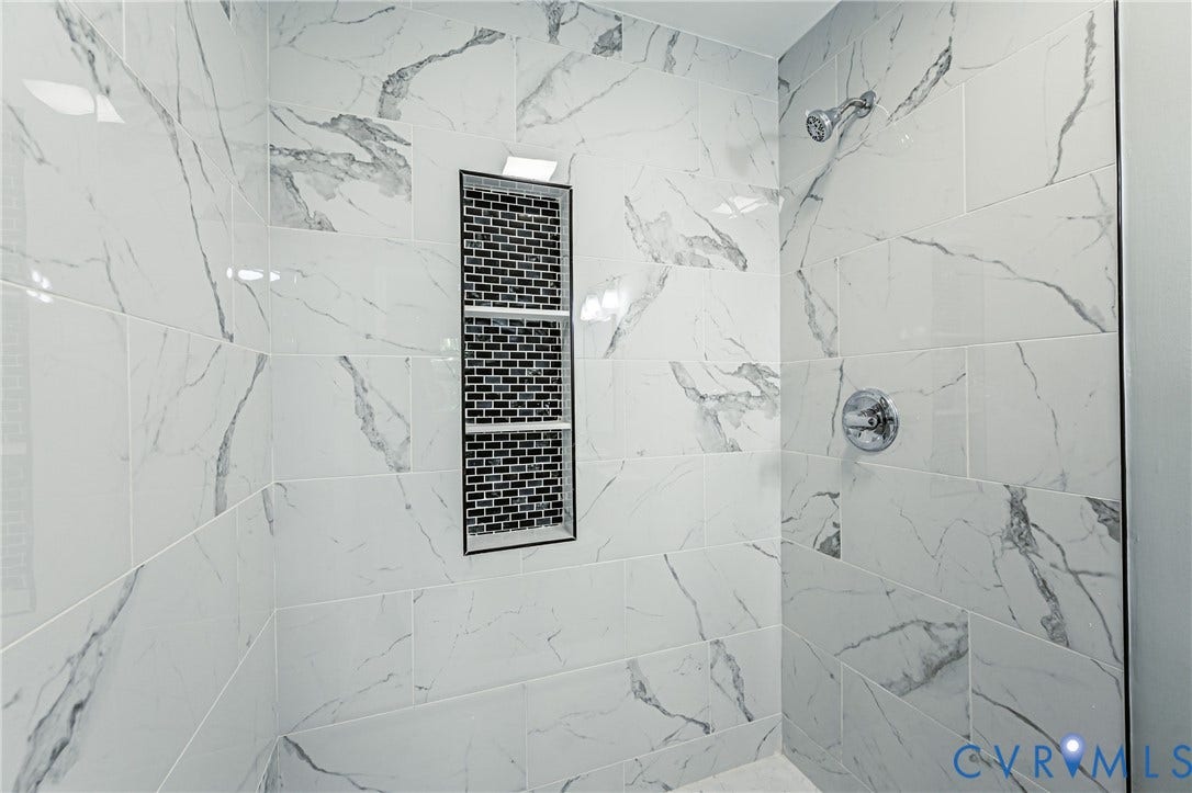 1724 Alaska Drive, Richmond, VA 23224 Shower stall featuring white and grey veined tile, a chrome showerhead, a built-in tiled niche with multiple shelves, and a chrome control knob