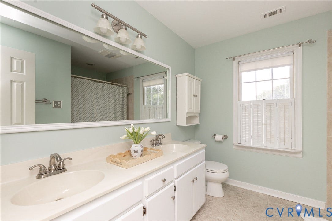 2120 Willowick Lane, Henrico, VA 23238 Double vanity with integrated sinks, white cabinetry, wall-mounted light fixture, window with privacy shutters, and a mounted storage cabinet