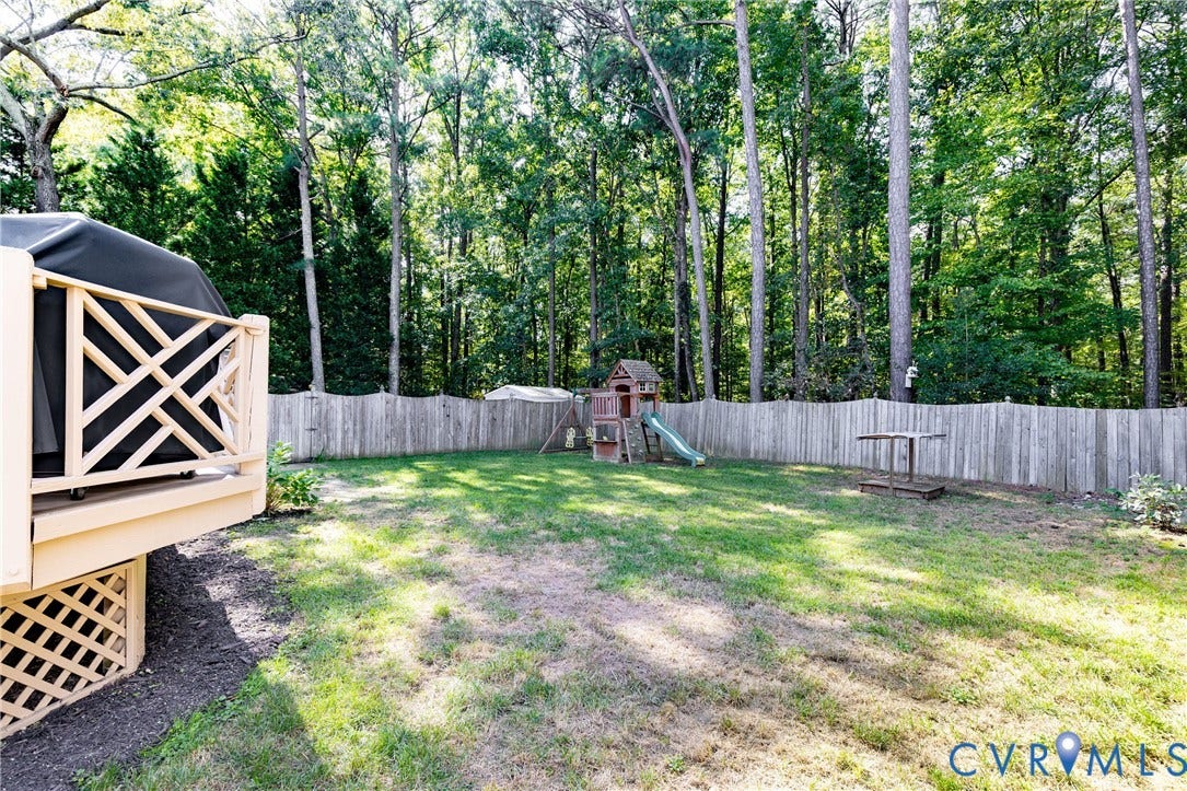 2120 Willowick Lane, Henrico, VA 23238 Spacious backyard featuring a wood fence, mature trees, and a raised wooden deck with lattice detailing