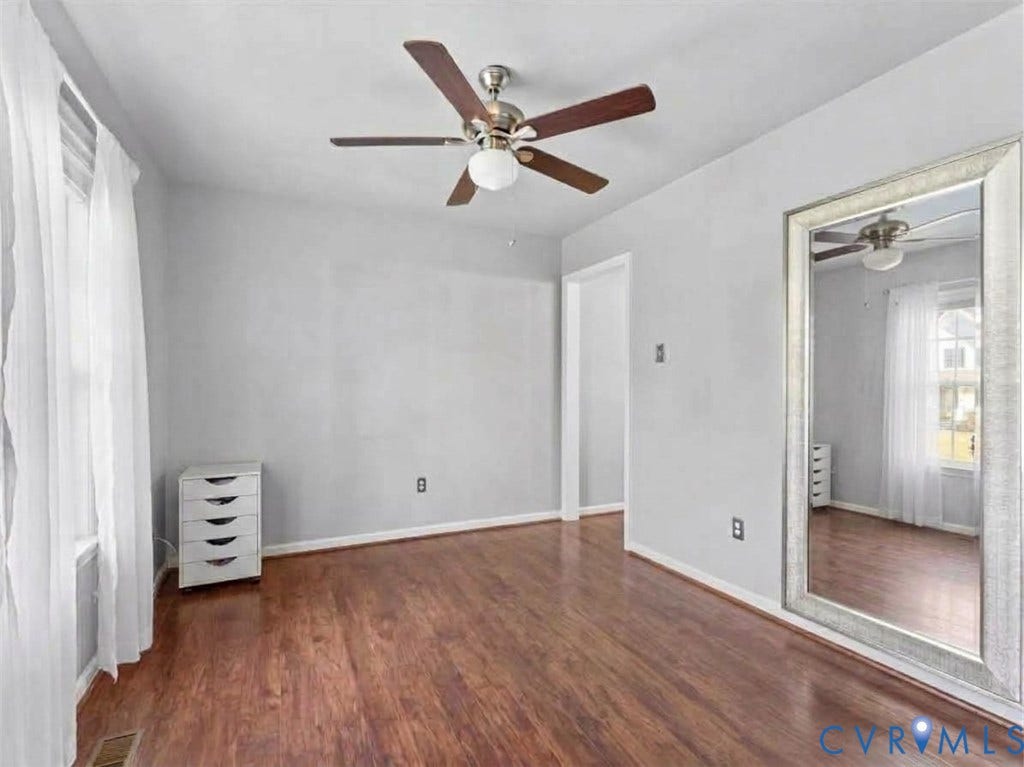 6507 Fairpines Road, North Chesterfield, VA 23234 Room is being used as a bedroom. Wood-finish flooring, ceiling fan with integrated lighting, and a doorway opening to kitchen and living room.Digitally edited