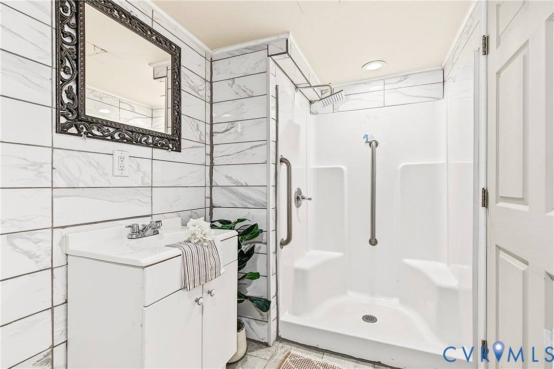 13310 Gladehill Road, Hidden Valley Estates, Chesterfield, VA 23831 White tiled walls with a decorative mirror, white vanity with integrated sink, and an accessible shower with grab bars