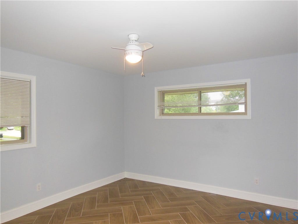 Herringbone-patterned tile flooring, white ceiling fan with integrated lighting, multiple windows with blinds, and light-toned wall finishes