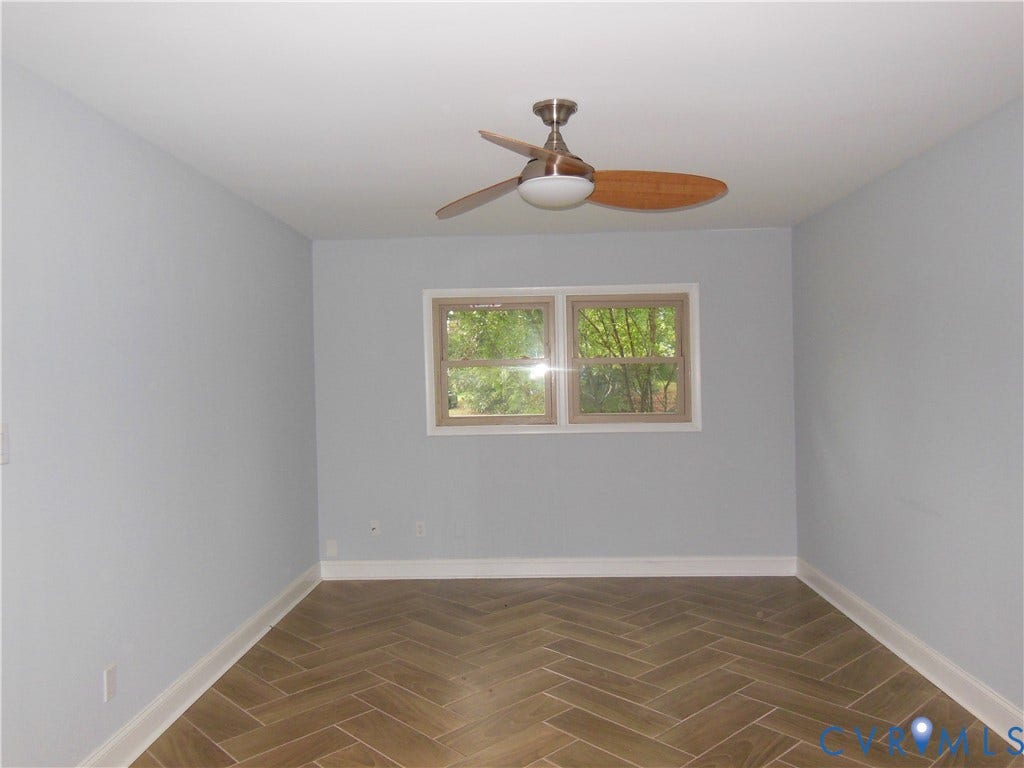 Room featuring herringbone-patterned tile flooring, white baseboards, two windows with light-colored frames, and a ceiling fan with wooden blades