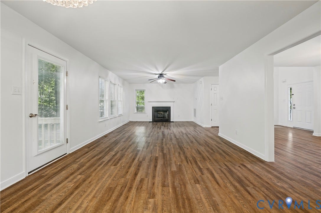 15724 Winding Ash Drive, Chesterfield, VA 23832 Spacious living area featuring wood-finish flooring, a fireplace with a white mantle, multiple windows with blinds, a ceiling fan, and a glass-paneled exterior door