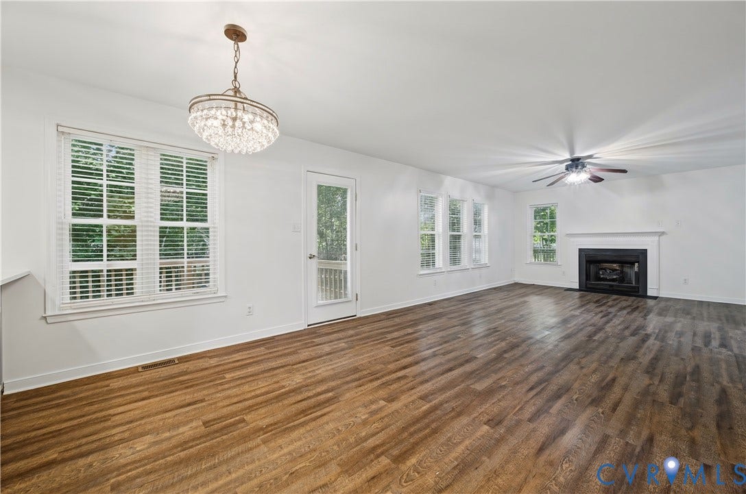 15724 Winding Ash Drive, Chesterfield, VA 23832 Spacious room featuring wood-finish flooring, multiple windows with blinds, a crystal-style chandelier, a ceiling fan, and a fireplace with a mantel