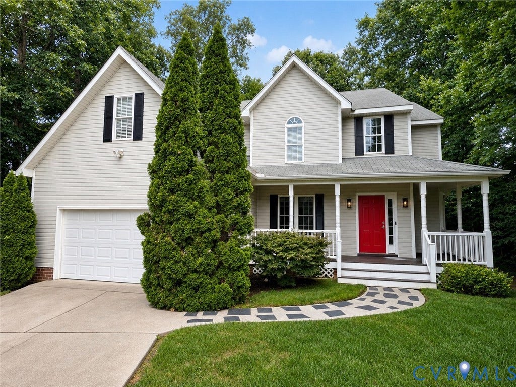 15724 Winding Ash Drive, Chesterfield, VA 23832 Two-story residence featuring light-colored siding, a covered front porch with white railings, a vibrant red entry door, a two-car garage, and a curved stone pathway