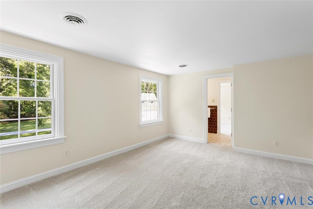 Light-colored carpeting, two paneled windows, and a doorway opening to an additional space