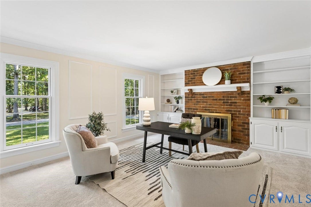 Brick fireplace with a gold-toned insert, built-in shelving, two large windows, panel molding, and light-toned carpeting