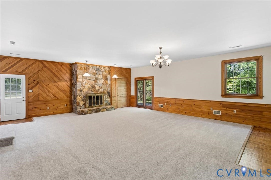 Spacious room featuring a stone fireplace, wood paneling, a chandelier, and a large window