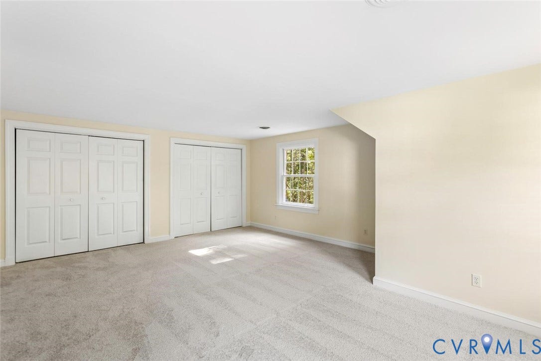 Light-colored carpeting, two sets of paneled bi-fold closet doors, and a single window with white trim