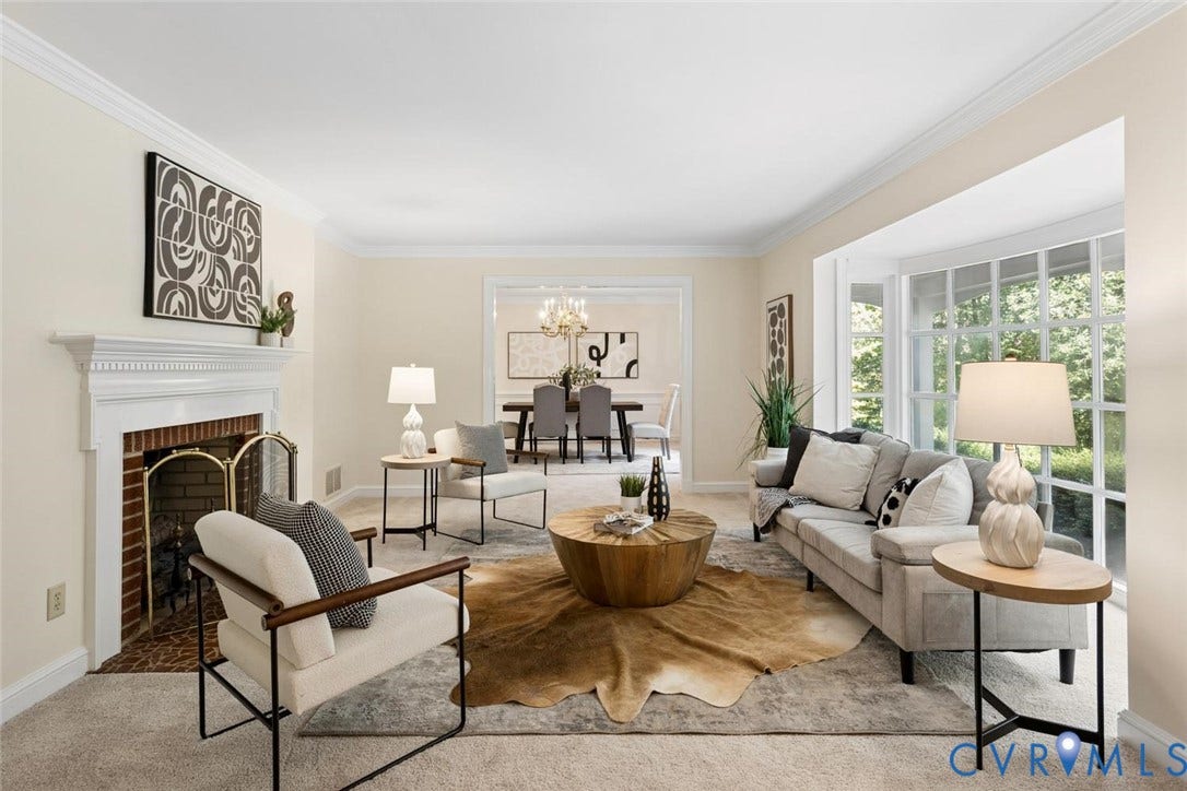 Living area featuring a brick fireplace with a white mantel, crown molding, a bay window, and a cased opening to an adjacent room