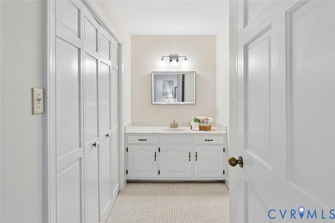 White paneled cabinetry with black hardware, white vanity with integrated sink, rectangular mirror, and sconce lighting