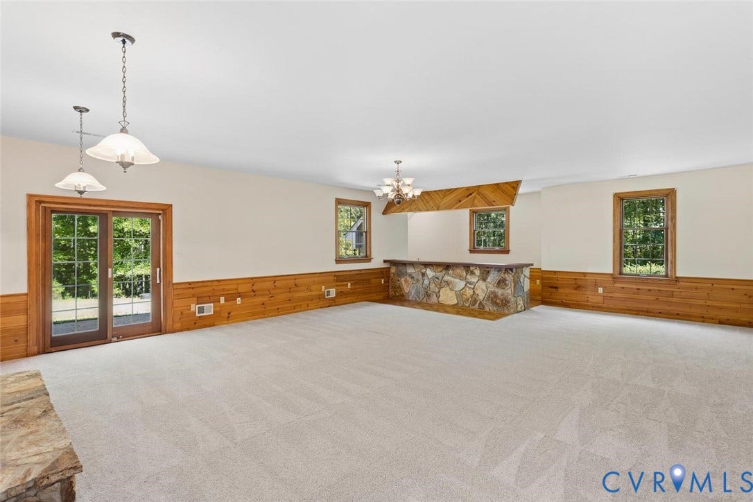 Spacious room with light-colored carpeting, a stone-clad wet bar, wood paneling, and multiple windows