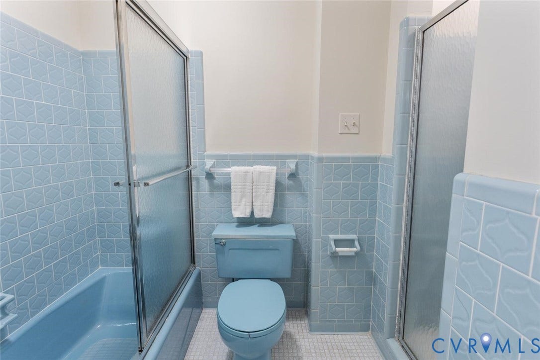 Blue tiled walls with decorative accents, matching blue toilet, and a combined tub/shower with sliding glass enclosure