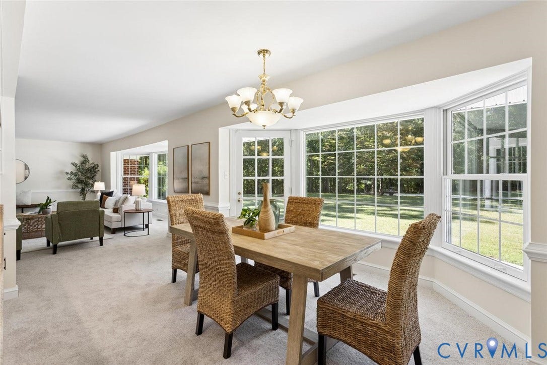 Expansive bay window, chandelier, white trim, light-colored walls, and carpet flooring