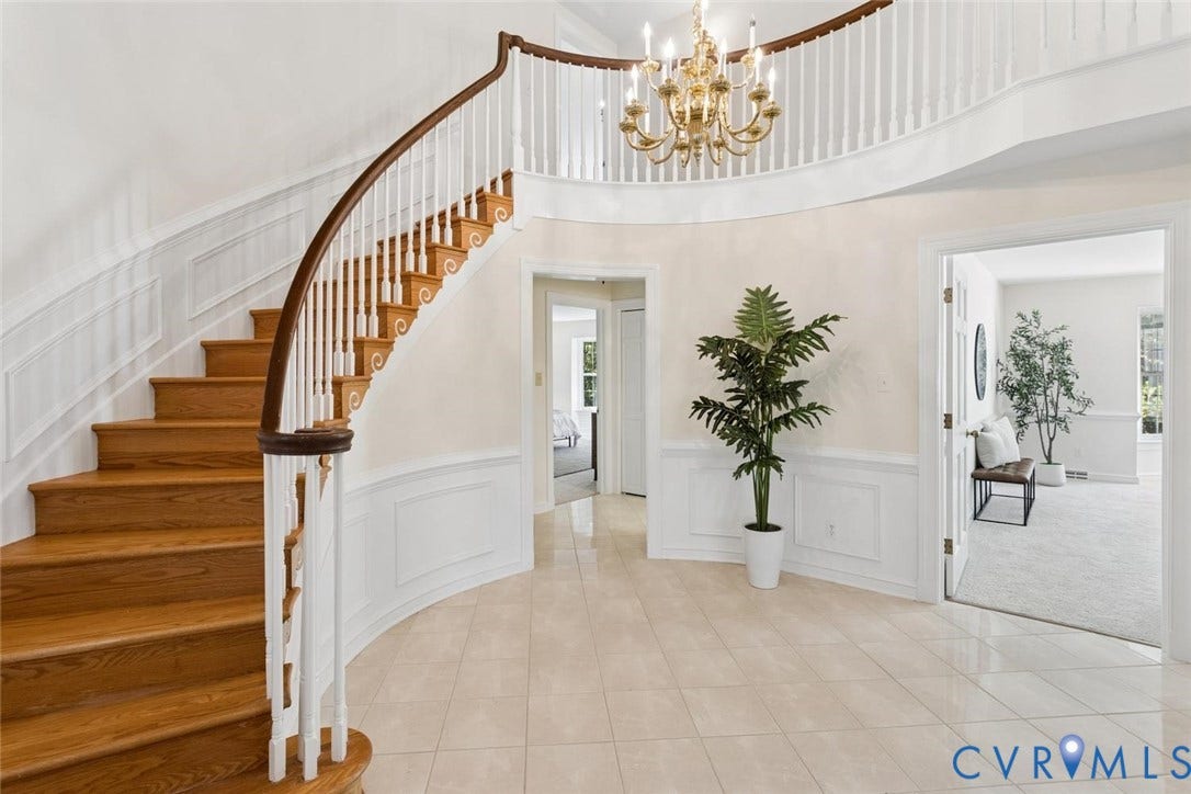 Grand foyer featuring a curved staircase with wood treads and a white balustrade, a two-story ceiling, and tile flooring