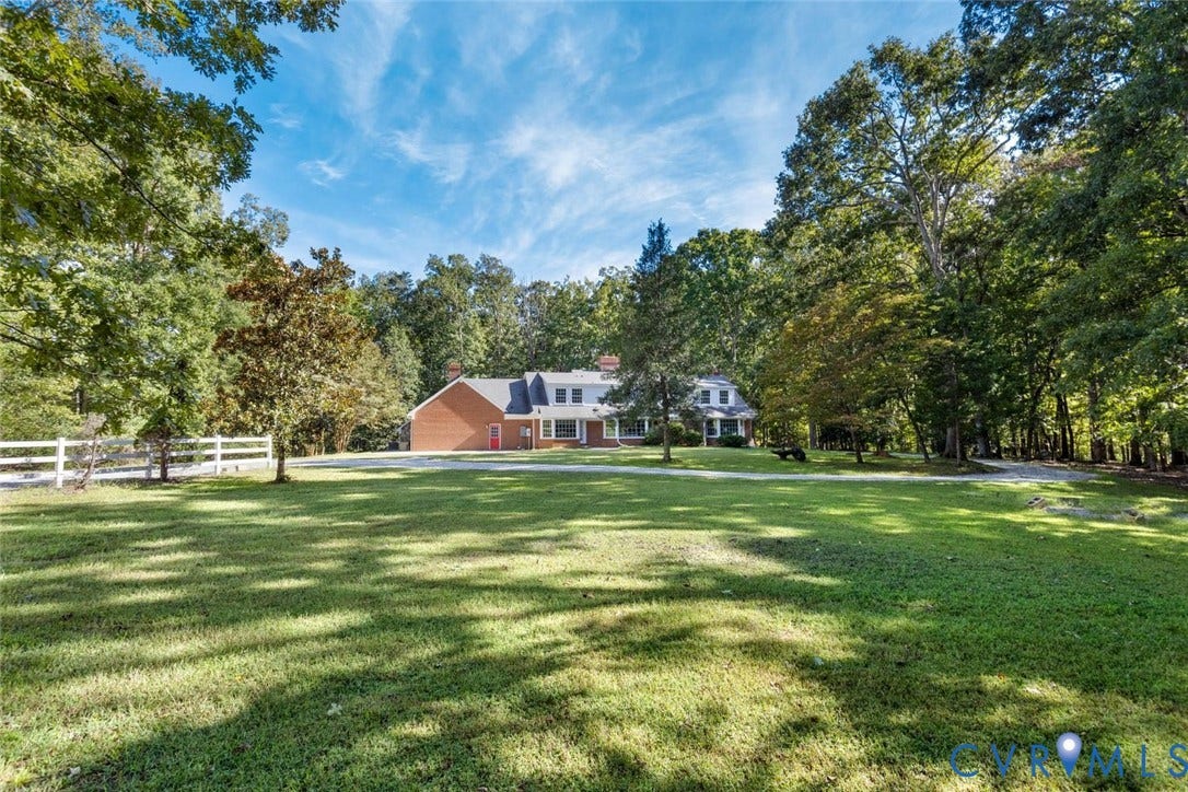 Expansive front lawn with mature trees and a white picket fence