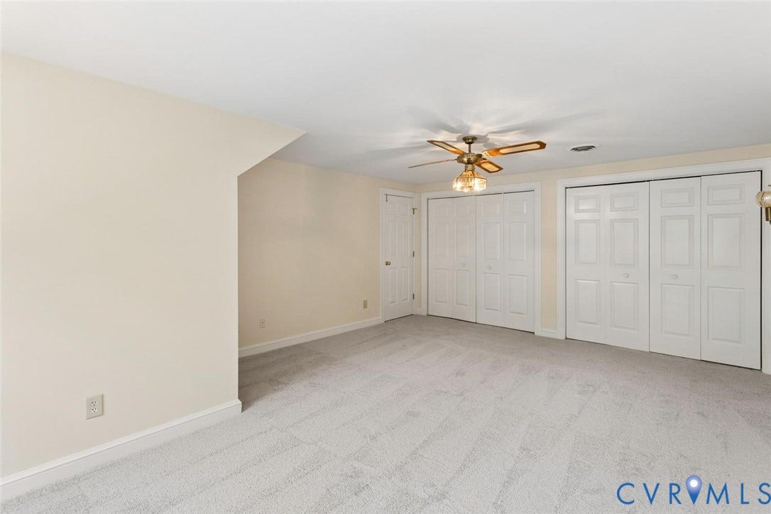 Wall-to-wall carpeting with multiple closet doors, a ceiling fan, and a solid-core door