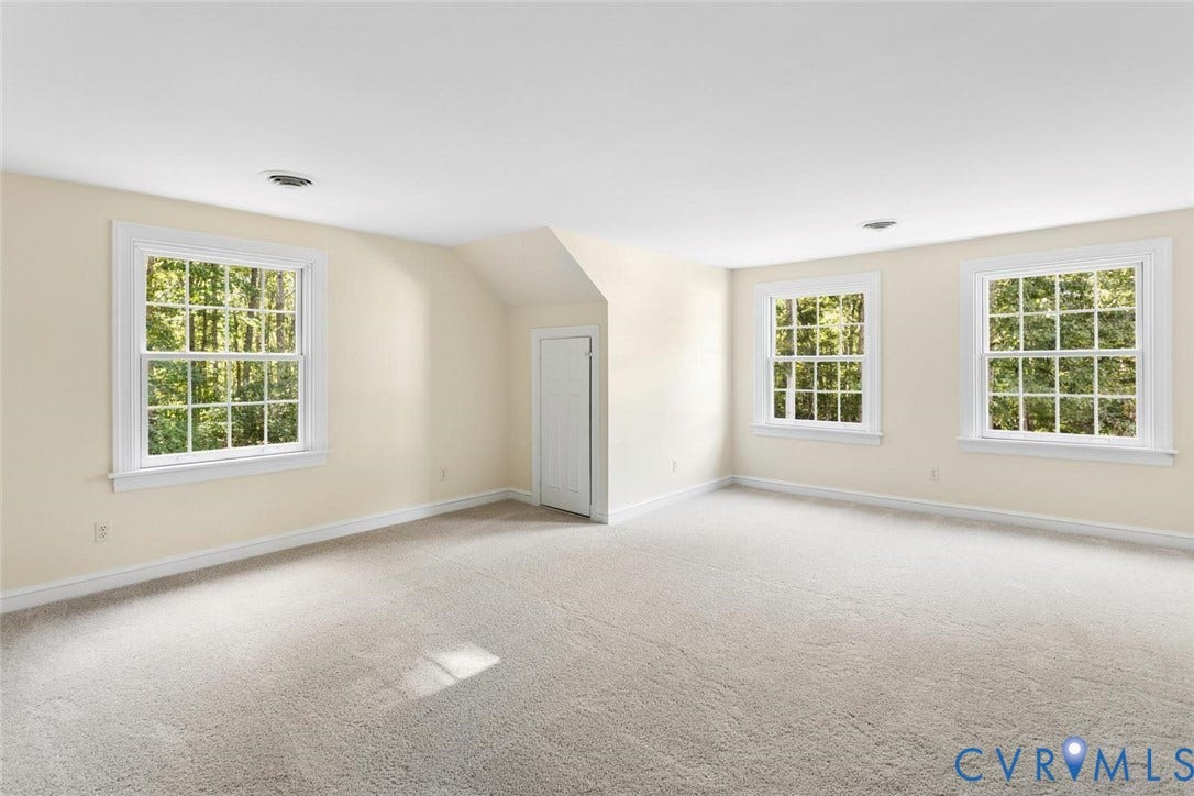 Expansive room featuring multiple windows with abundant natural light, neutral carpeting, and a built-in closet with a paneled door