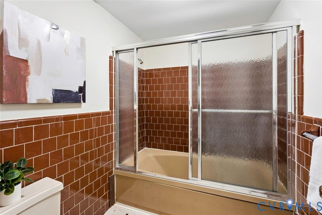 Bathtub with sliding glass shower doors, surrounded by brown subway tile