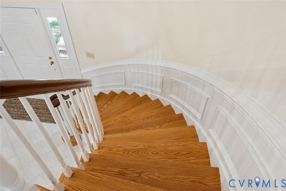 Curved staircase with wood-finish treads and white risers, featuring a wood-finish handrail and white balusters