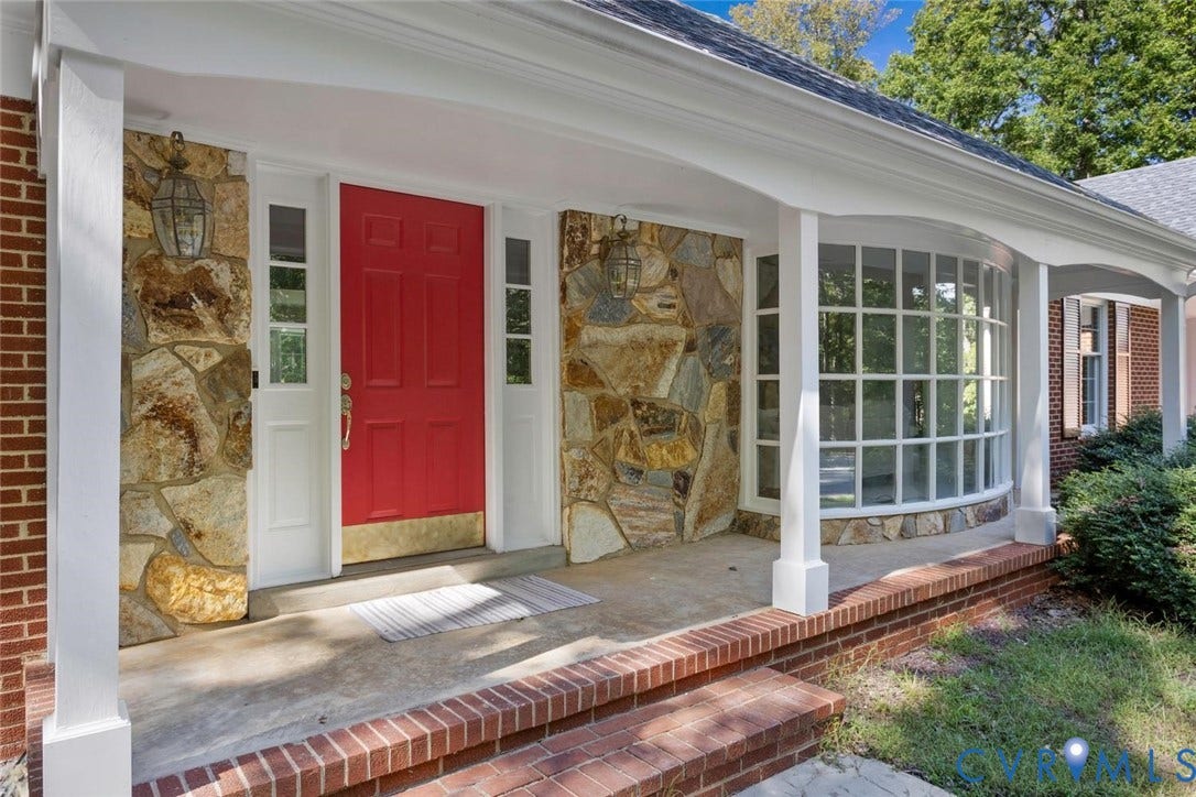 Covered front porch featuring a prominent red entry door, natural stone accents, and a curved bay window