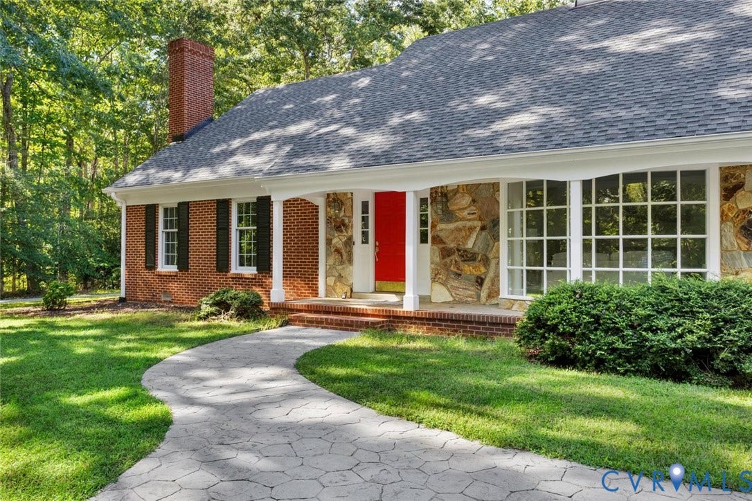 Brick and stone facade featuring a red entry door, white columns, and multi-pane windows