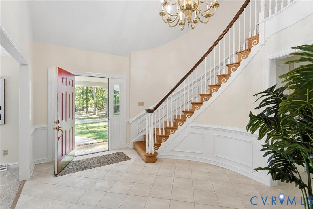 Foyer with tile flooring, curved staircase featuring wood treads and white risers, and decorative wainscoting