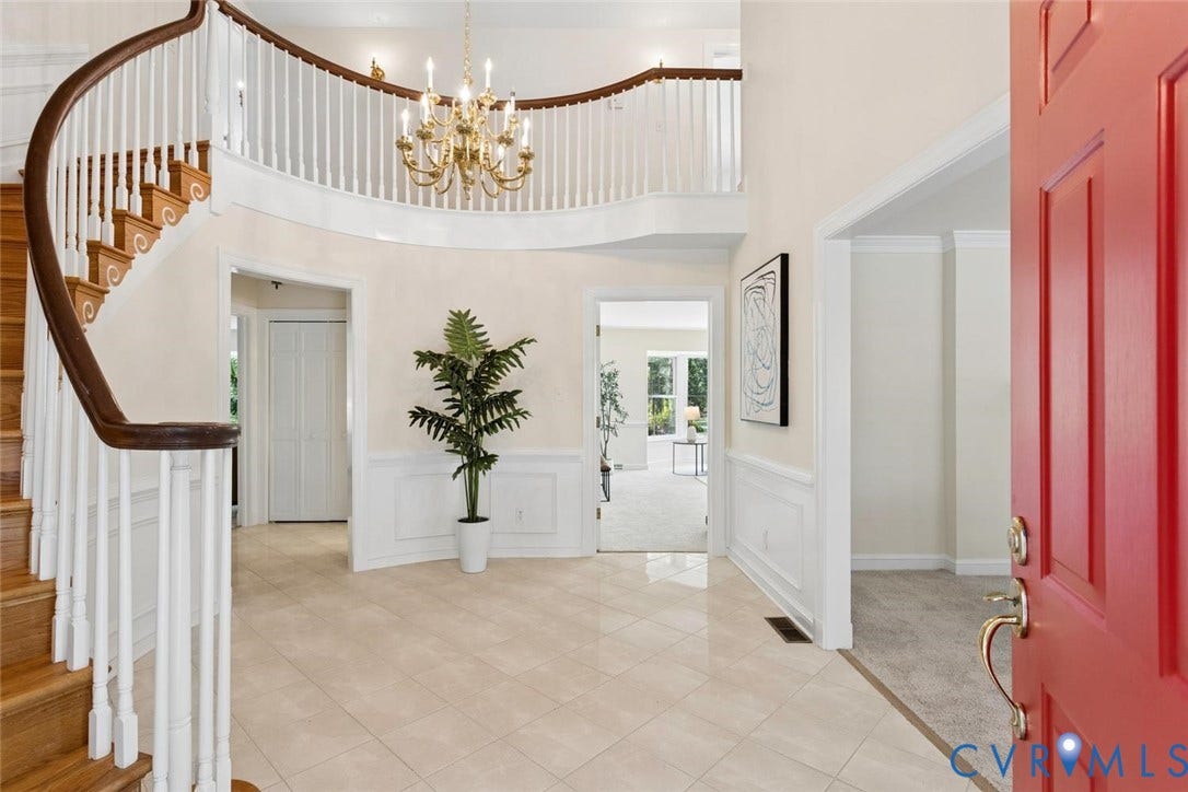 Two-story foyer featuring a grand curved staircase with wood treads, a chandelier, wainscoting, and tile flooring