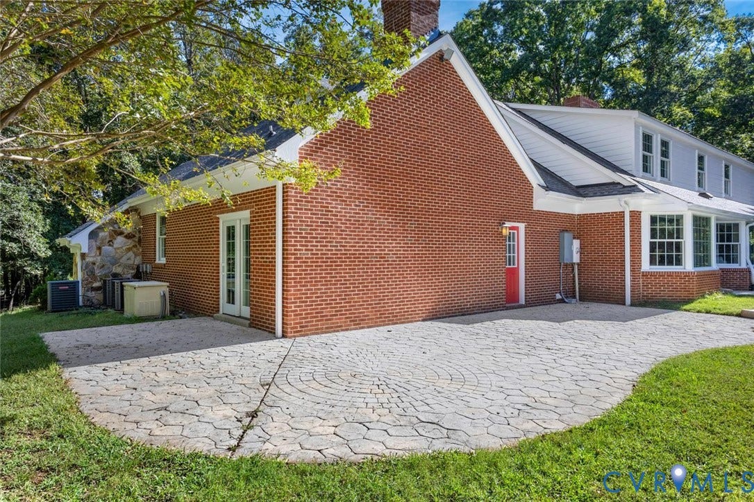 Expansive paver patio with a circular pattern, brick exterior, stone accent wall, double-pane glass doors, and multiple windows