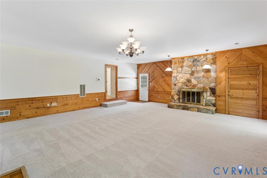 Spacious room featuring a stone fireplace, wood paneling, and wall-to-wall carpeting
