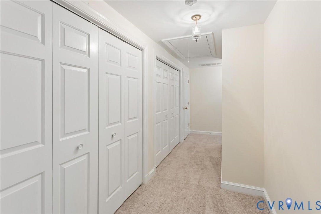 Carpeted hallway with multiple paneled bi-fold doors, neutral wall paint, and a ceiling-mounted light fixture