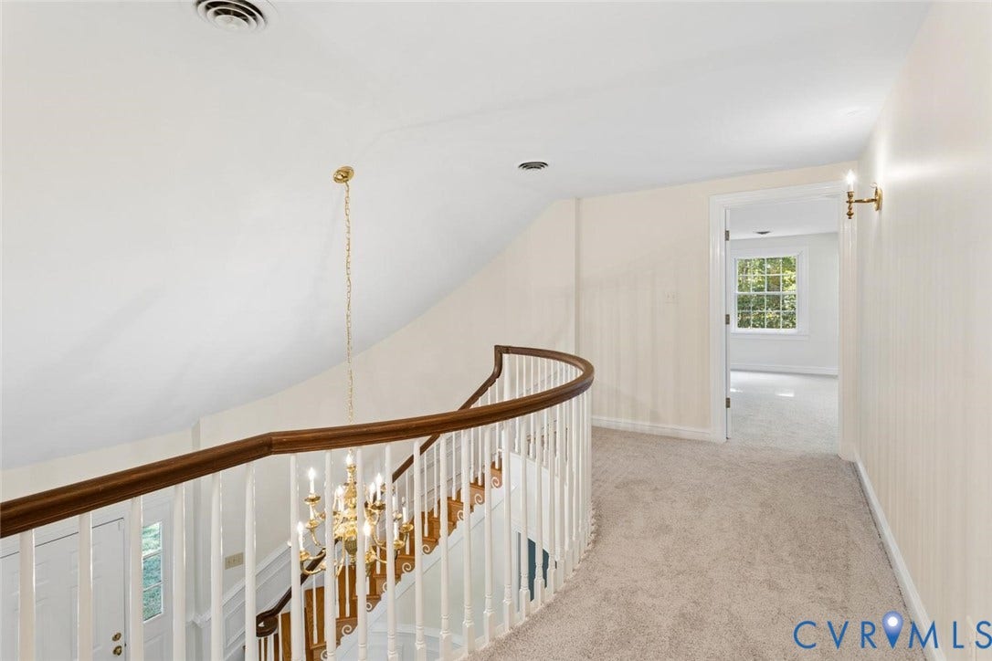 Curved staircase with wood handrail and white spindles, complemented by a brass chandelier and wall sconce